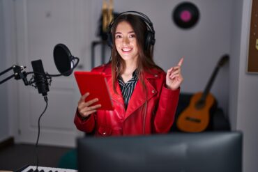 Young brunette woman singing song using microphone smiling happy pointing with hand and finger to the side