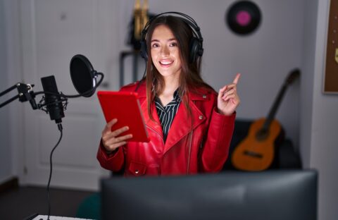 Young brunette woman singing song using microphone smiling happy pointing with hand and finger to the side